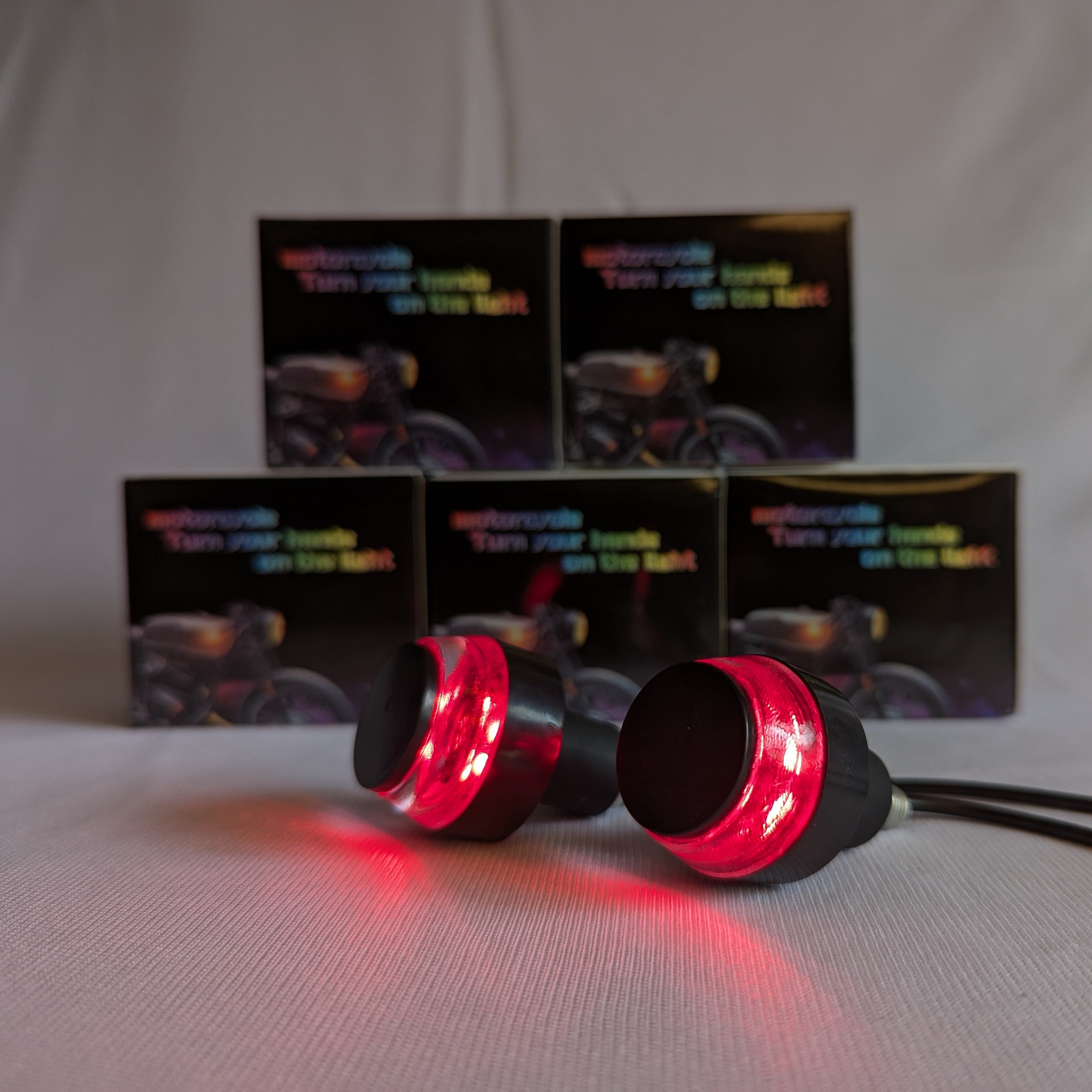 Red LED lights with black casings on a white background, with motorcycle-themed boxes in the background.