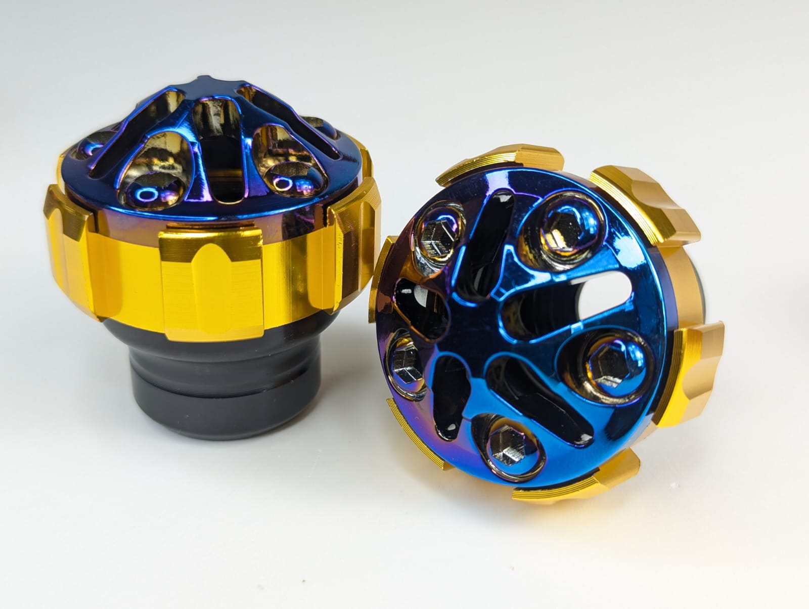 Two metallic metal parts with blue and gold finish on a white background